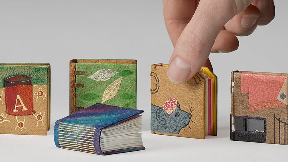 A selection of the books created in celebration of 100 years of Queen Mary’s Dolls’ House. A selection of miniature books with a hand about the pick one up.