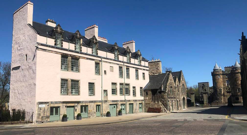The Abbey Strand buildings now used as a Learning Centre. Cream building on the left with a street in front. To the right are the gate and entrance to the Palace of Holyroodhouse.