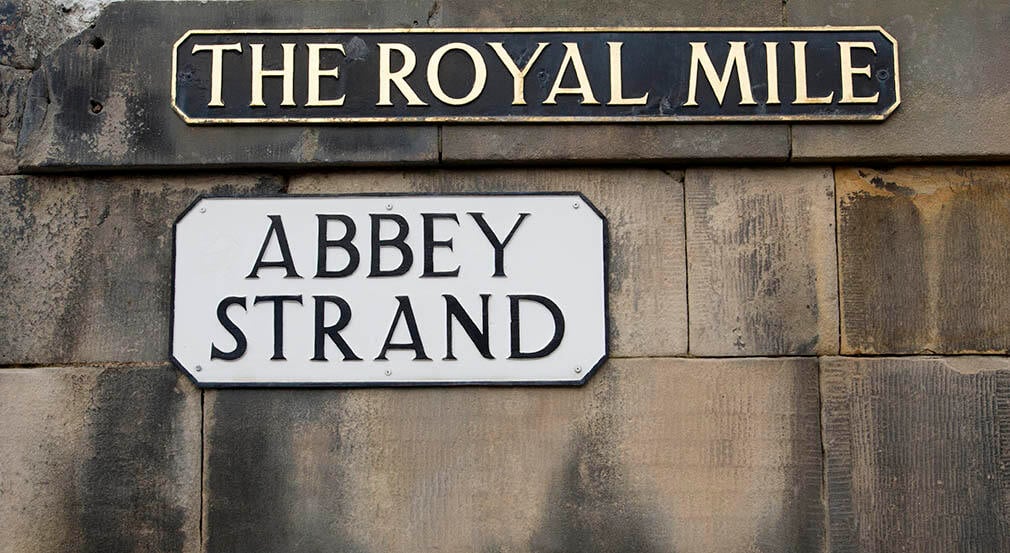 Abbey Strand sign. A image of a brick wall with a street sign with the text 'The Royal Mile' and another sign with the text 'Abbey Strand'.